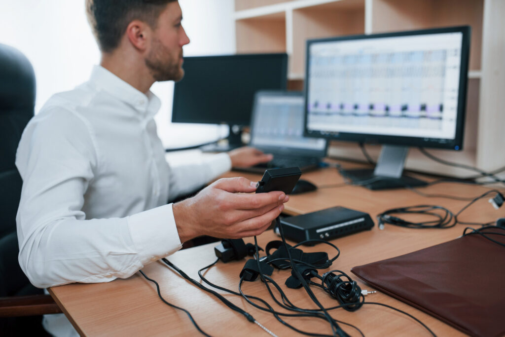 A technician sitting at a desk holding a sensor device and analyzing data from ultrasonic methane detectors.
