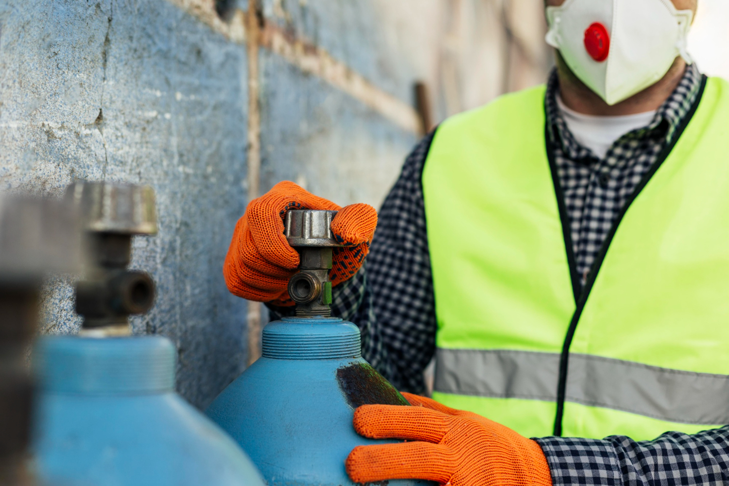 Worker in safety gear turning a blue cylinder valve, illustrating the safety steps for how to detect methane gas leaks.