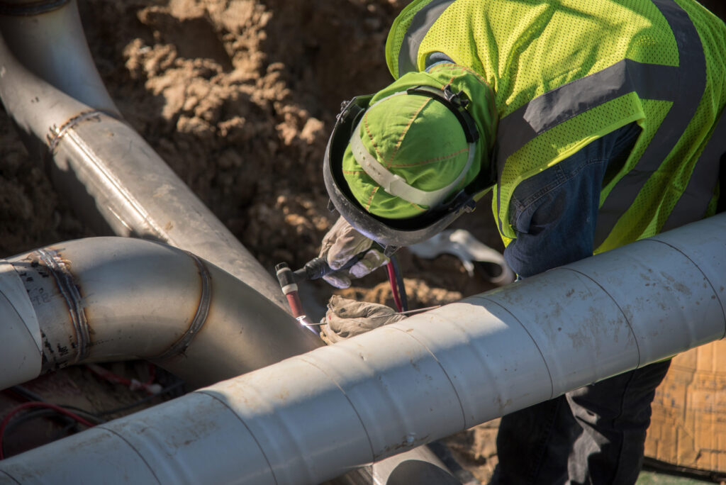 Construction worker welding an underground pipeline during maintenance work supporting Methane Leakage Detection and infrastructure integrity.
